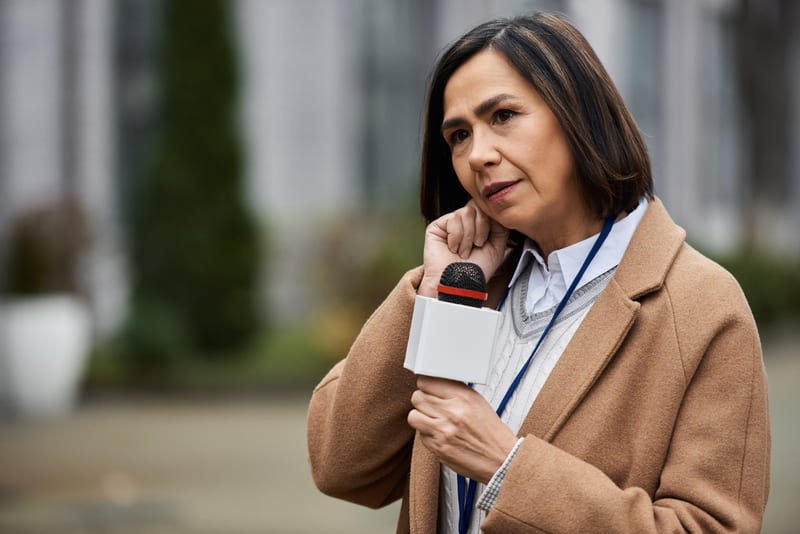 multiracial-female-journalist-beige-coat-reports-news-outside-cool-afternoon (1)